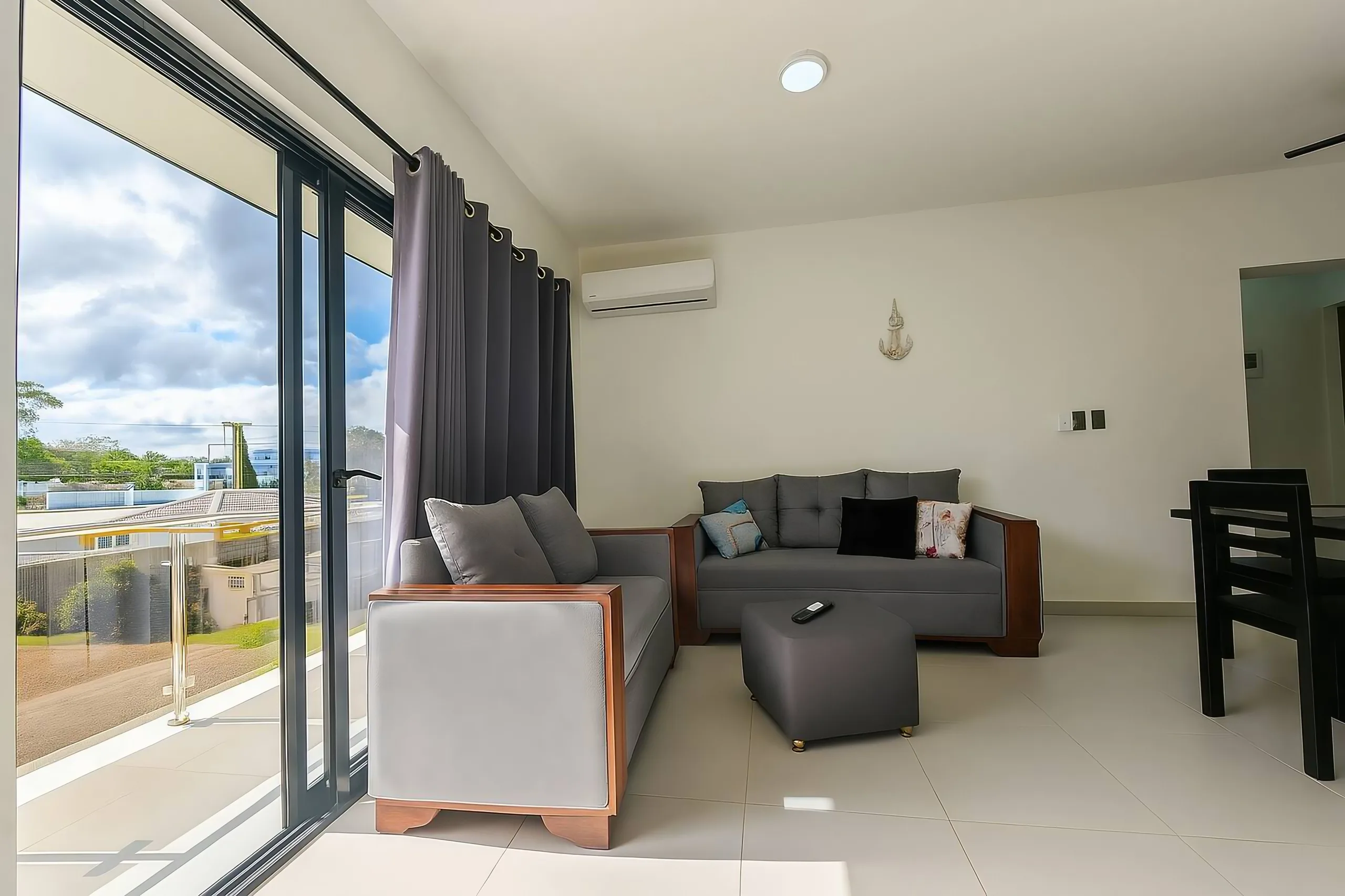 La pièce est meublée de deux canapés contemporains à structure en bois et tissu gris clair. L’un est un deux places et l’autre un trois places, tous deux garnis de coussins décoratifs aux tons doux et d’un coussin noir.